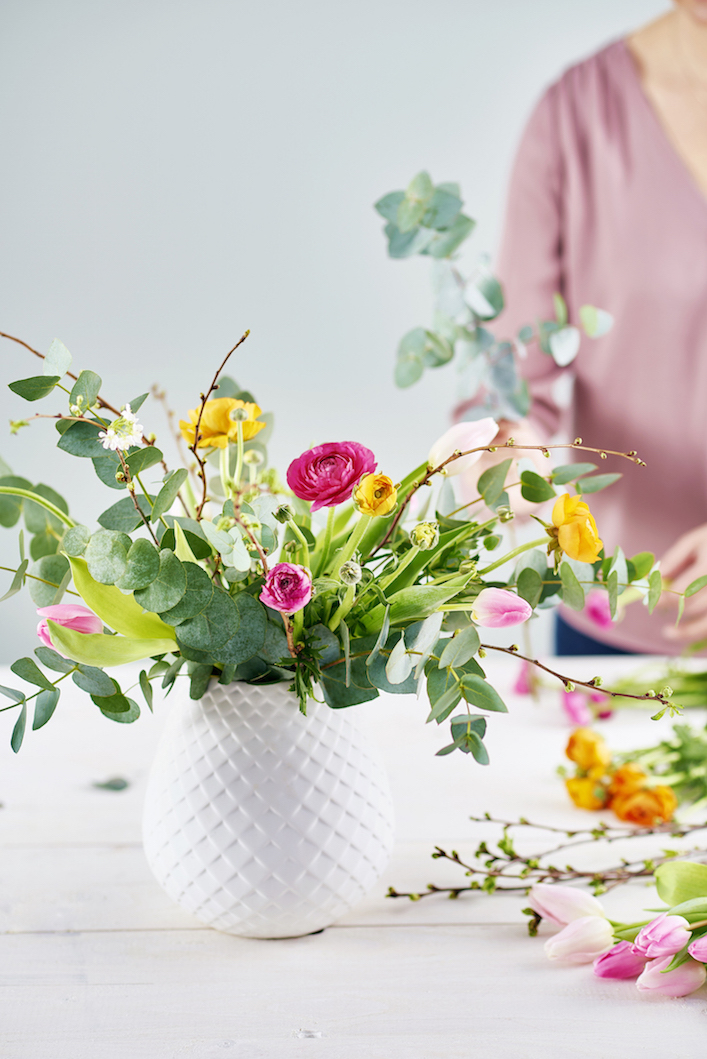 A vibrant bouquet of pink, yellow, and white flowers in a textured white vase.