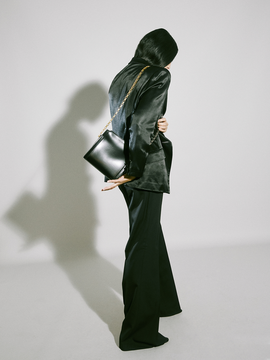 Woman in black satin suit and flared pants, holding a black clutch bag.