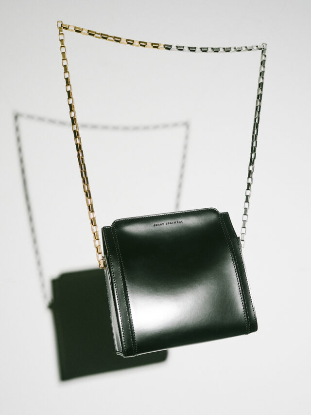 A dark green leather purse with a gold and silver chain strap hangs against a white background.