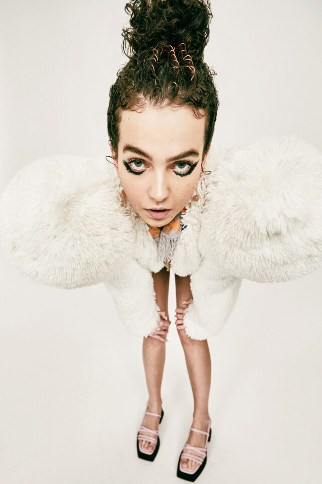 Woman with dramatic eye makeup and fluffy white coat, looking down.