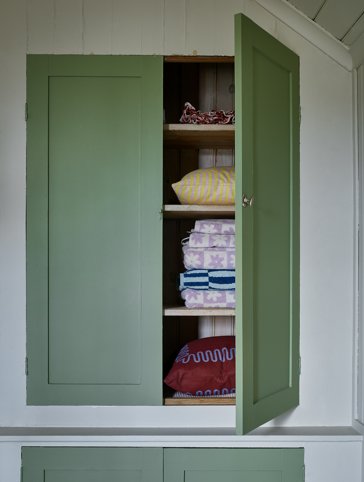 Green cabinet with open door revealing shelves of colorful pillows and folded towels.