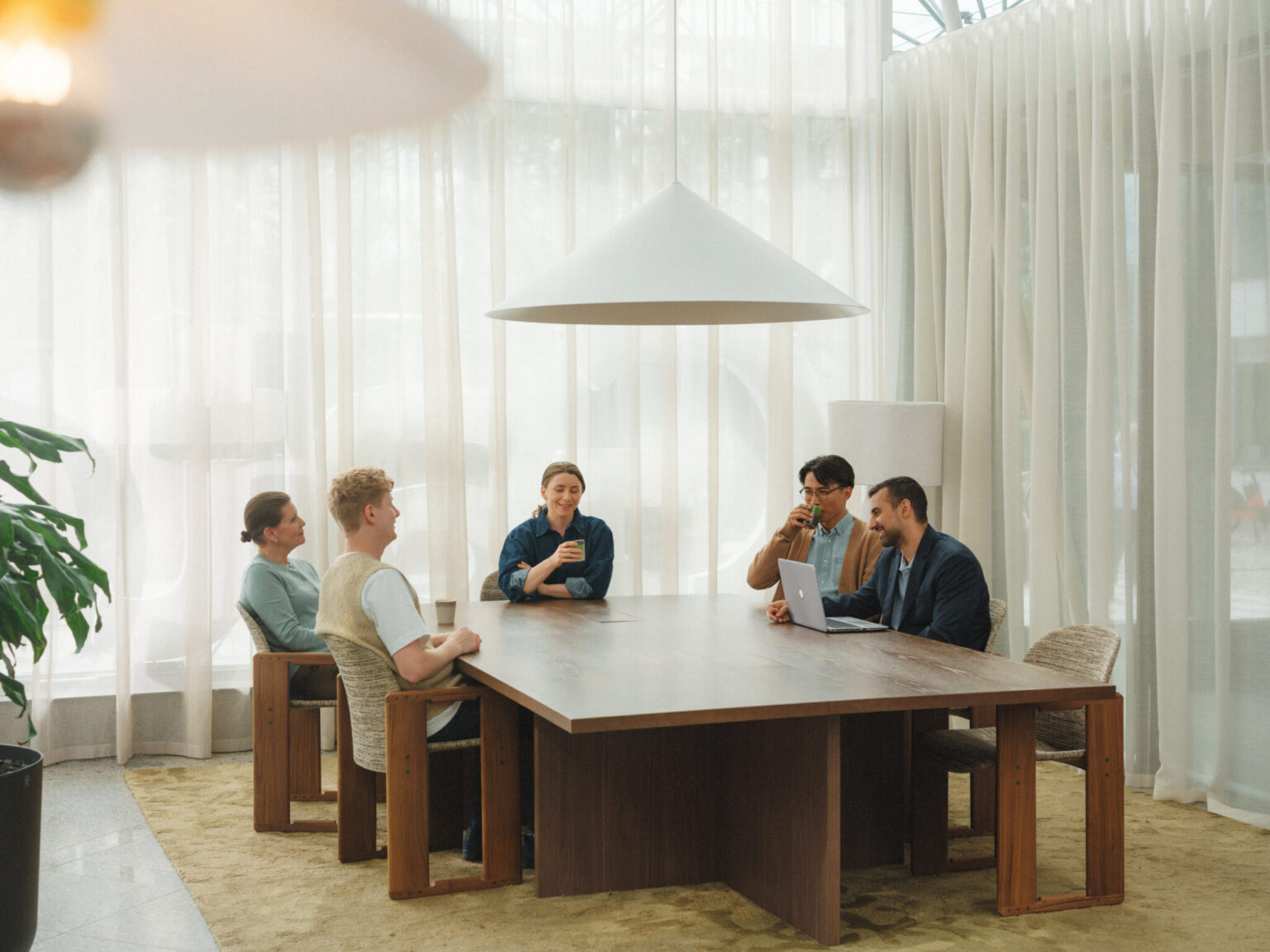 Five people in a meeting around a large wooden table.